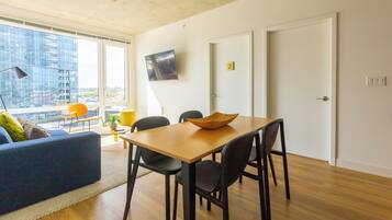 A modern living space with a dining area, a sofa, a TV, and a city view.