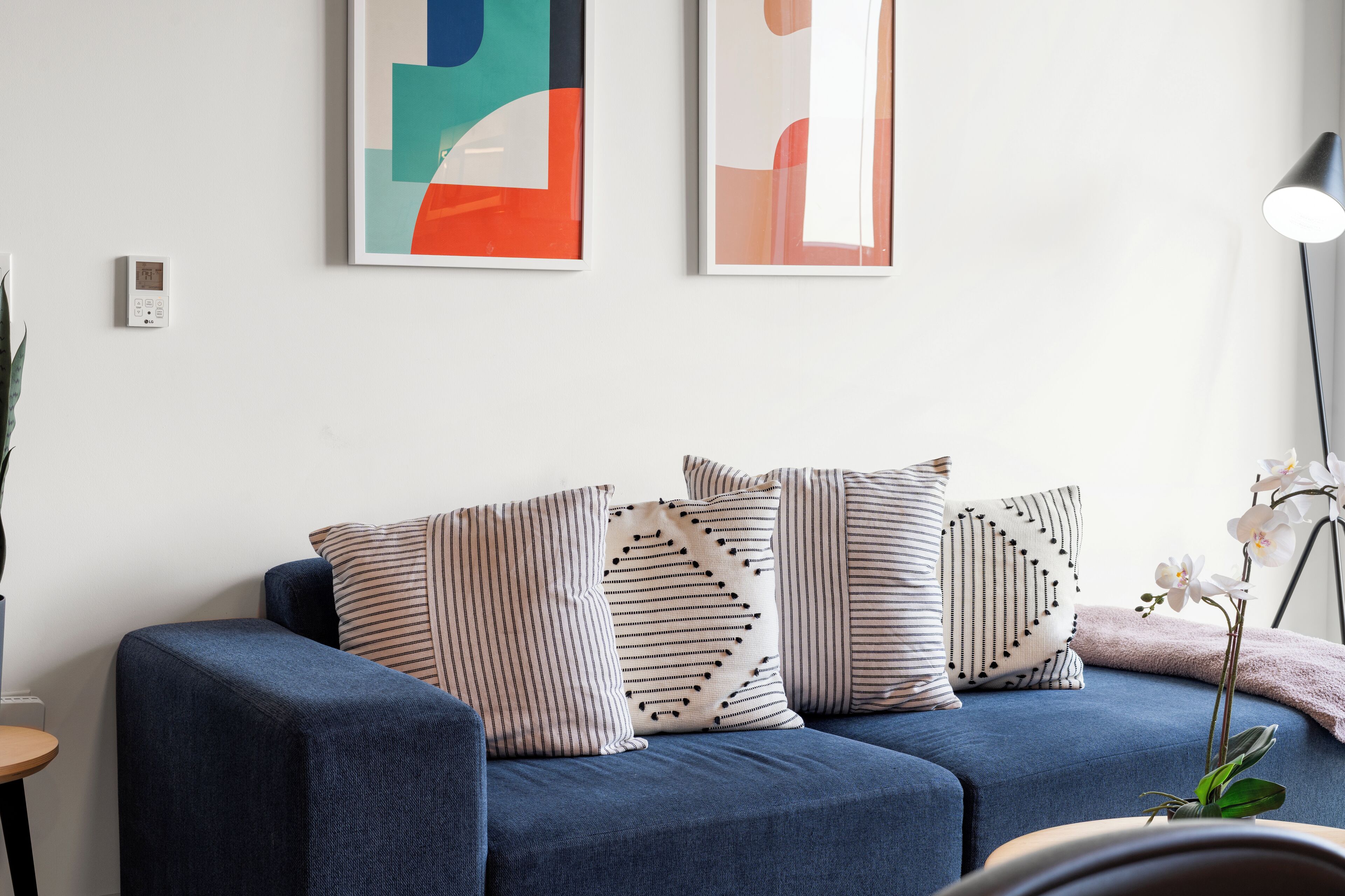 Una sala de estar moderna con un sofá azul, cojines estampados con motivos geométricos y rayas, arte abstracto en la pared y una lámpara de pie.