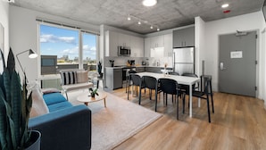 Un appartement moderne comprenant une cuisine, un coin repas et un salon. Il dispose d’une grande fenêtre, d’un canapé, d’une table à manger et d’une cuisine équipée d’un four à micro-ondes et d’un réfrigérateur.