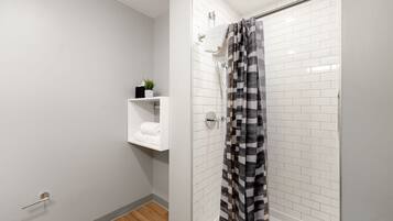 Un baño moderno con azulejos blancos tipo metro, ducha con cortina a rayas negras y blancas, un estante con una planta y un perchero.