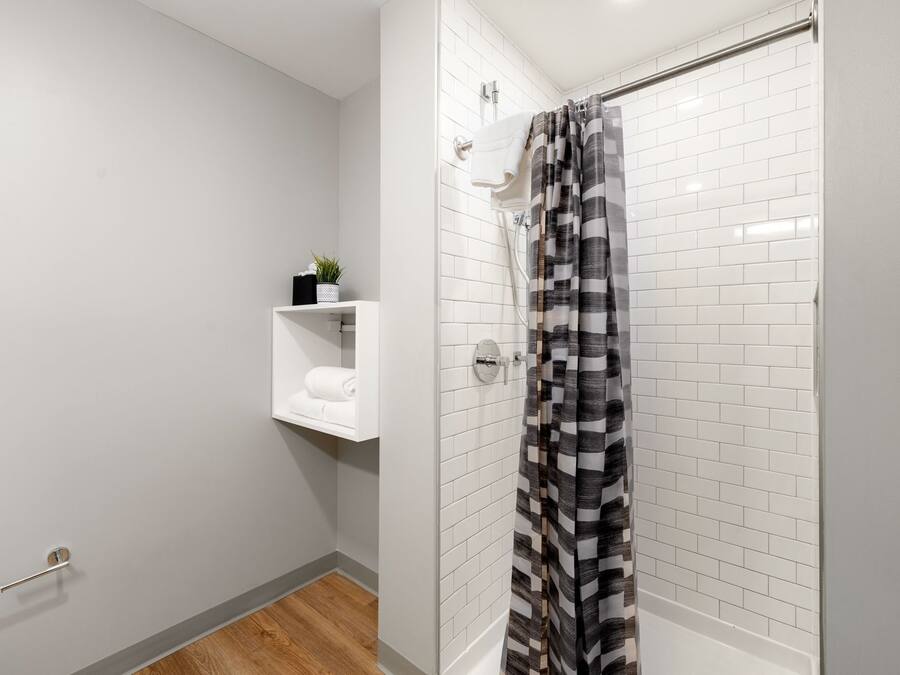 Un baño moderno con azulejos blancos tipo metro, ducha con cortina a rayas negras y blancas, un estante con una planta y un perchero.
