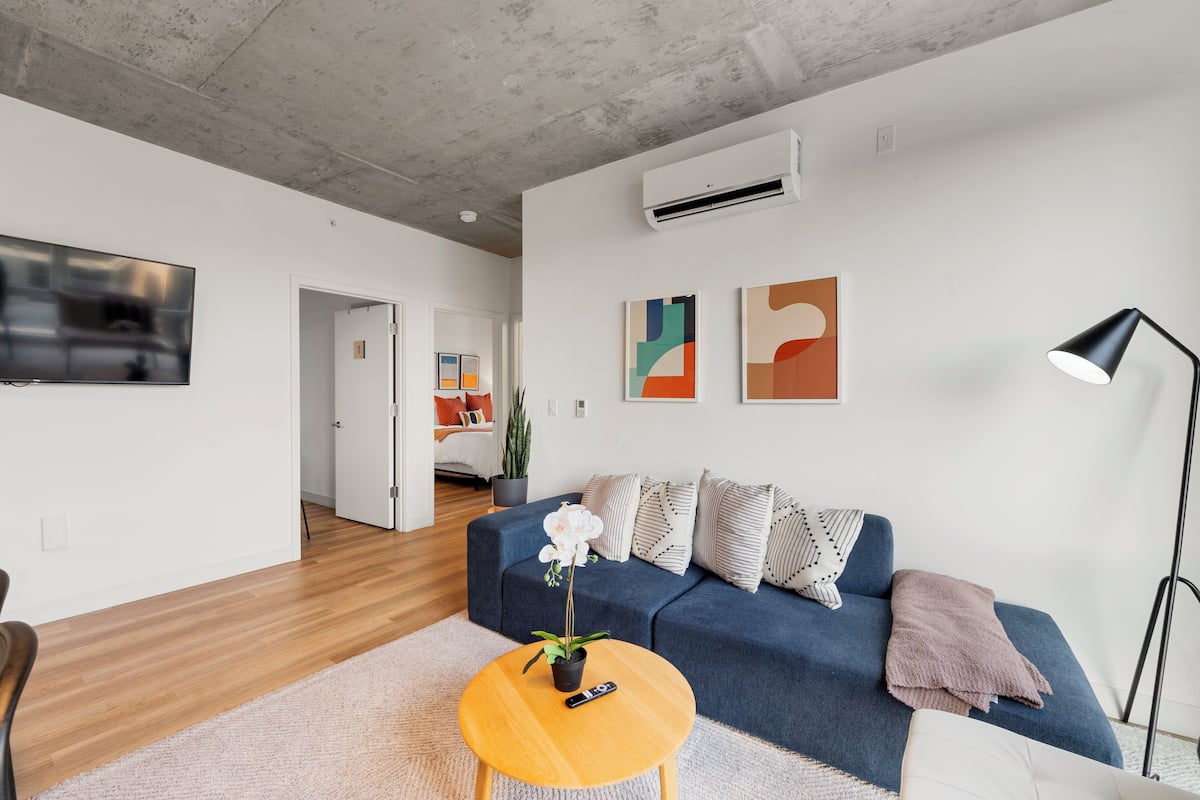 A modern living room with a blue sofa, a round wooden coffee table, and a TV mounted on the wall.