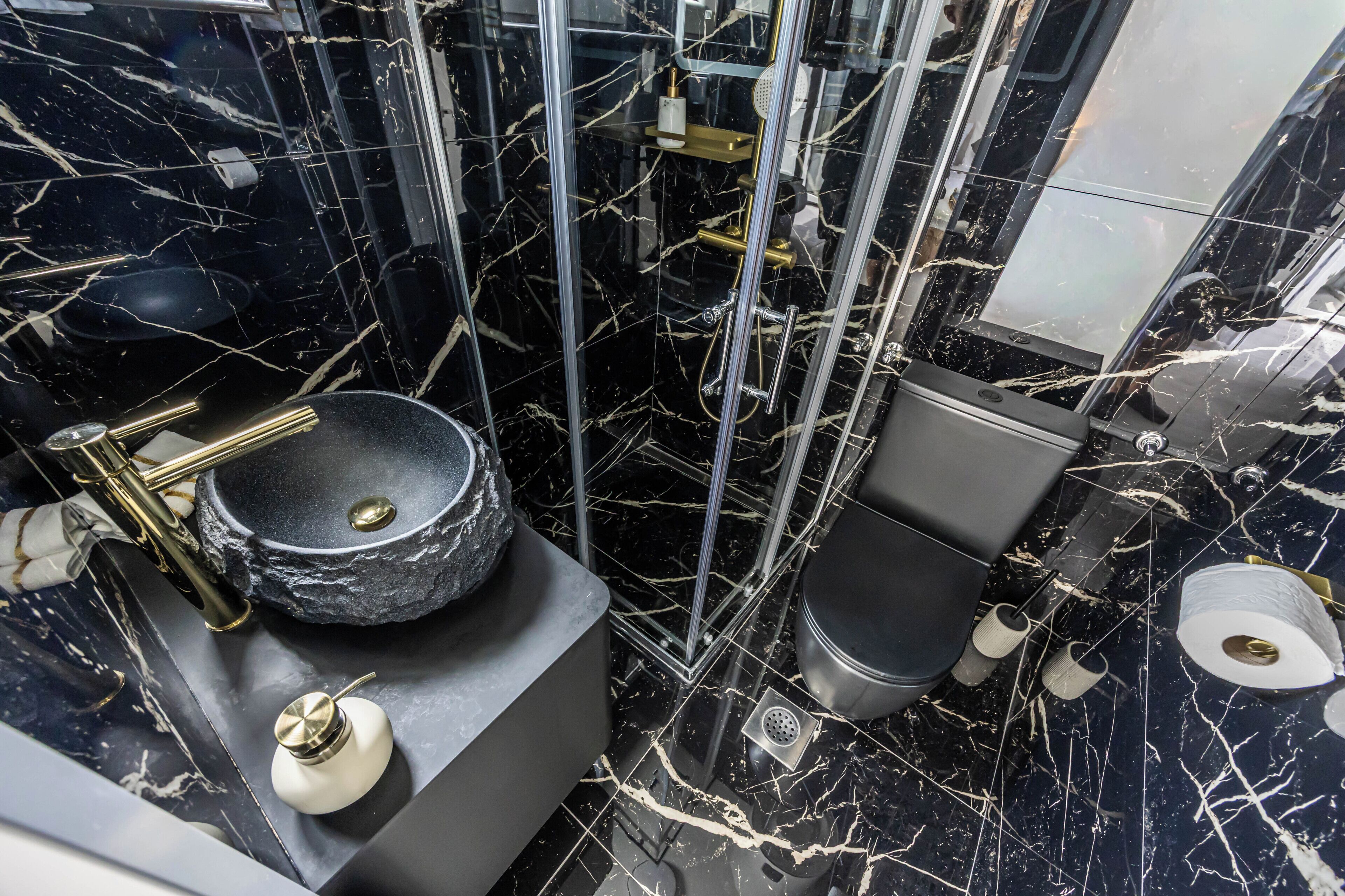 A bathroom with a black marble floor, a round sink, a toilet, and a shower enclosure.