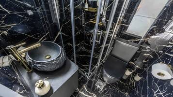 A bathroom with a black marble floor, a round sink, a toilet, and a shower enclosure.