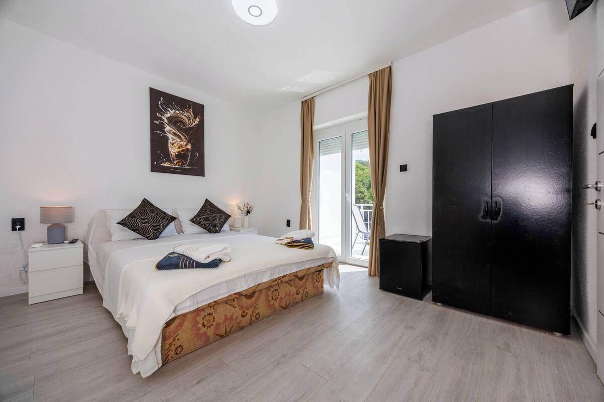 Un dormitorio con una cama, una mesita de noche, un armario negro y una puerta que da a un balcón.