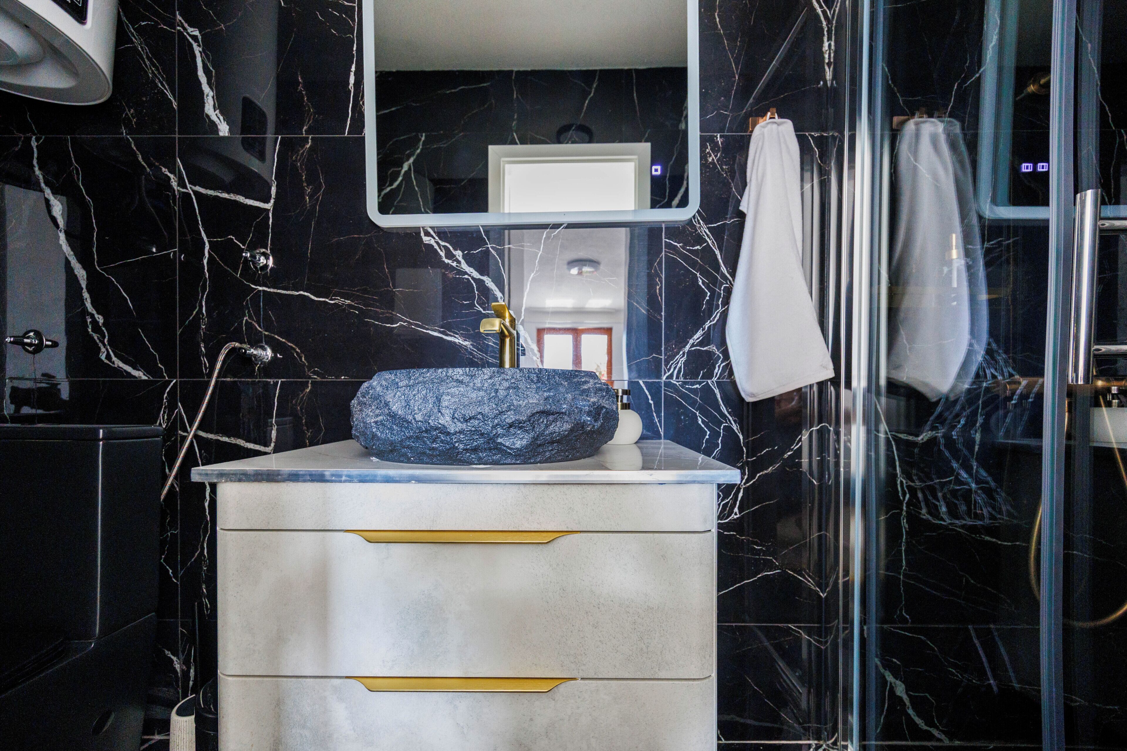 Un baño con lavamanos de mármol, un espejo y una cabina de ducha con paredes de vidrio.