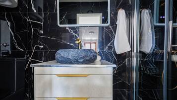 Un baño con lavamanos de mármol, un espejo y una cabina de ducha con paredes de vidrio.
