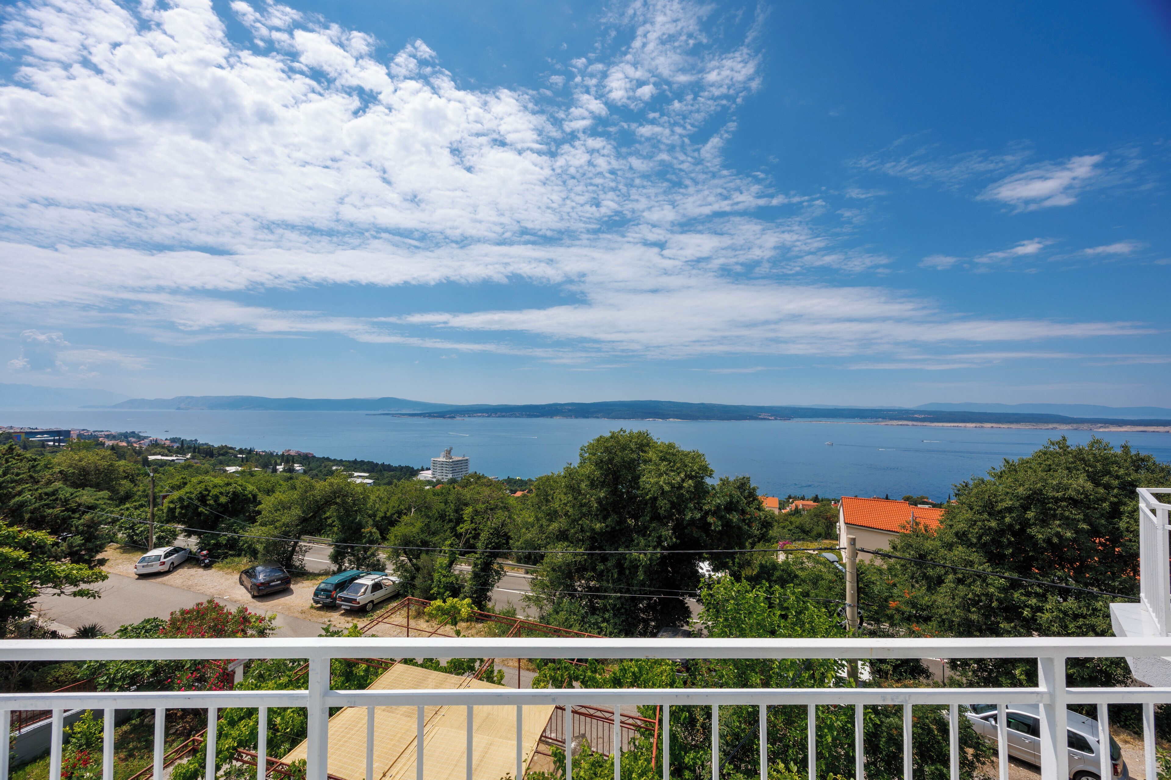 A balcony with a view of a body of water, trees, and distant buildings.