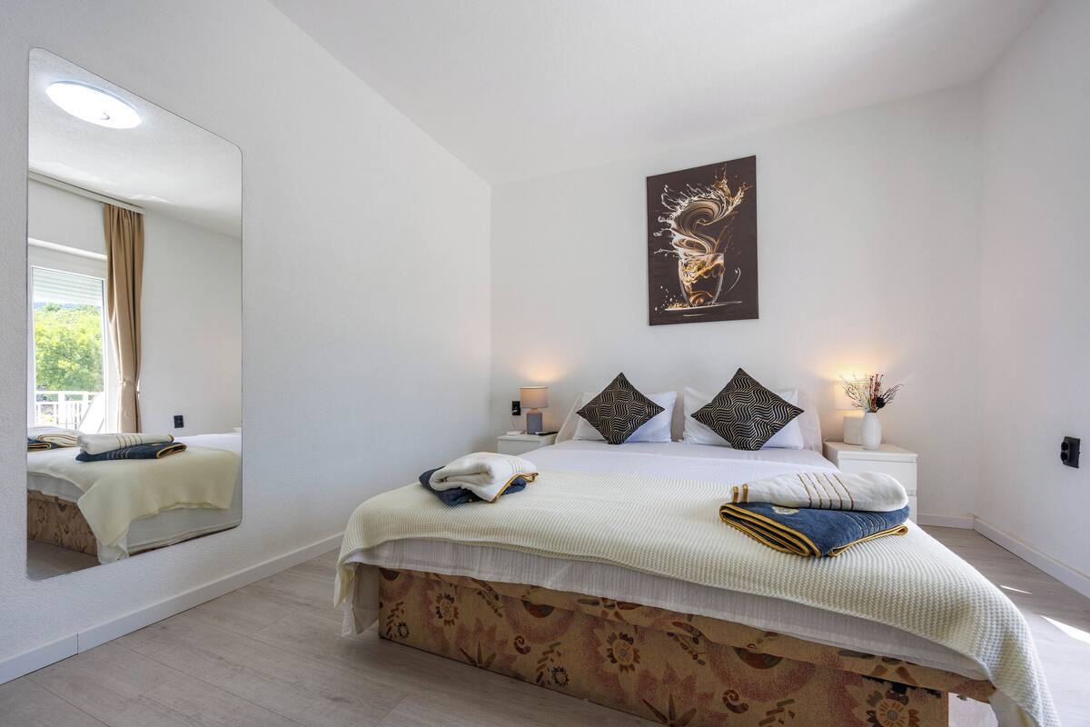 Un dormitorio con un espejo grande, una cama con colcha estampada, un cuadro abstracto colgado en la pared y lámparas de noche.