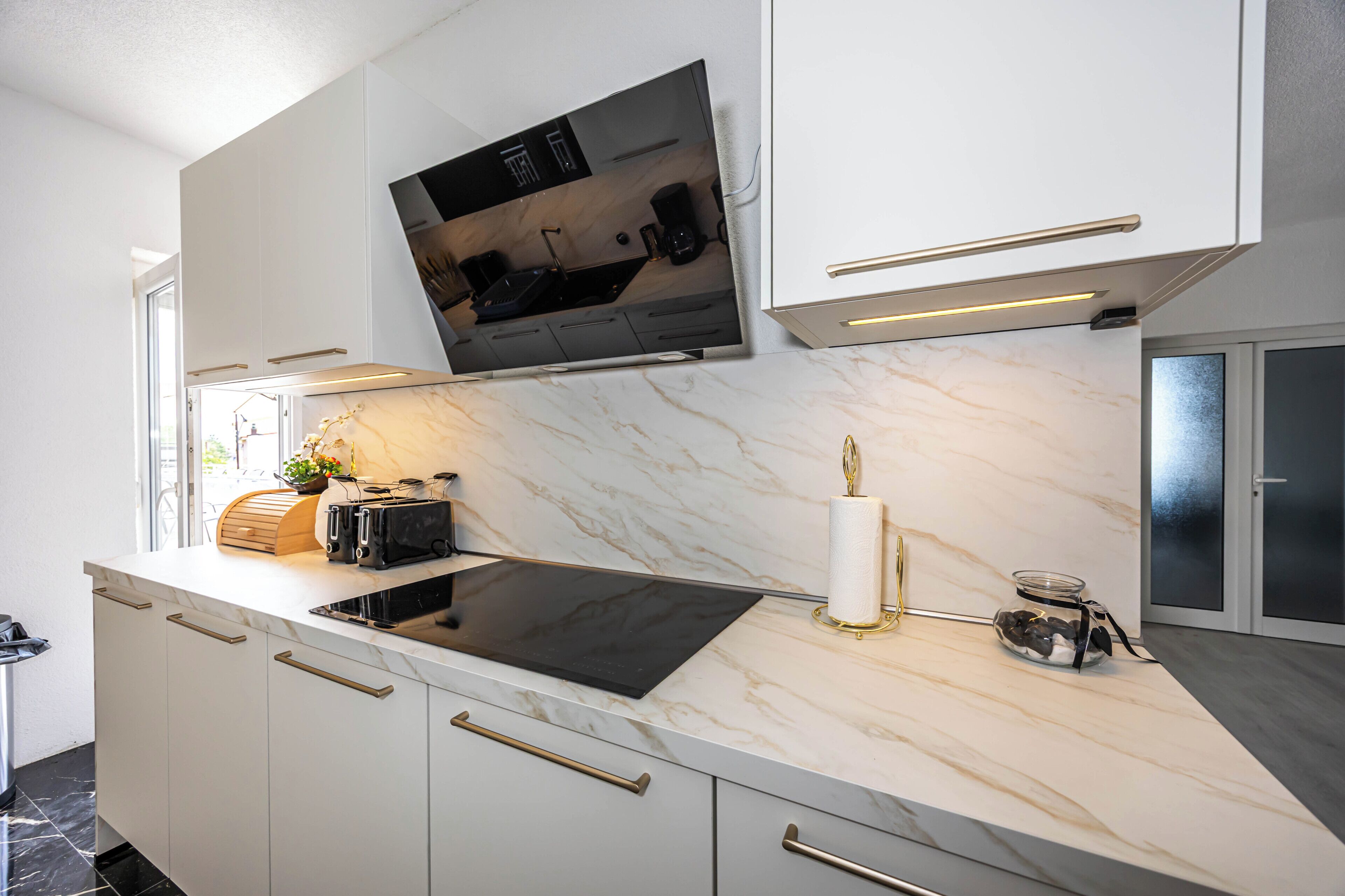 A modern kitchen with a flat-screen TV, marble countertop, and built-in cabinets.