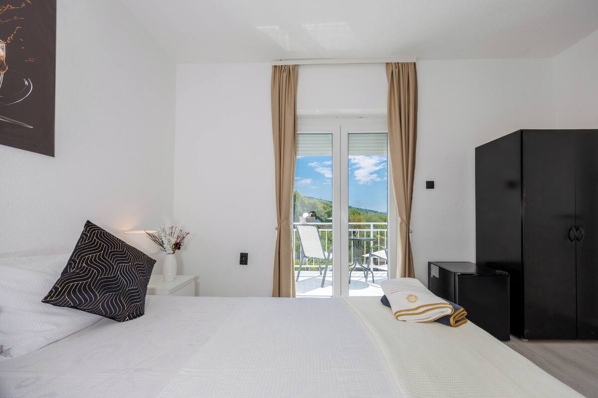 Una habitación de hotel con cama, mesita de noche, armario negro y balcón con vistas.