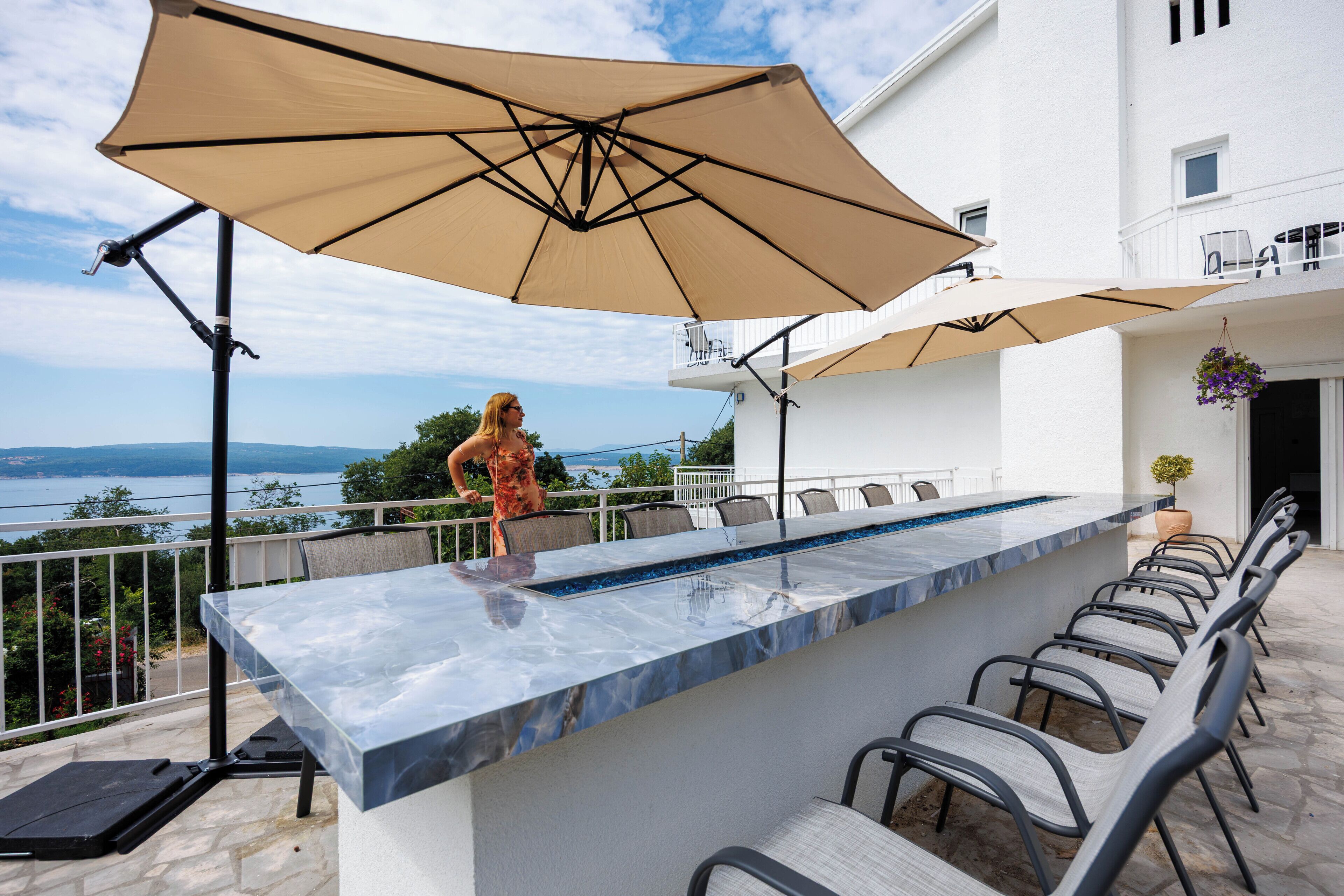An outdoor bar area with a marble countertop, multiple chairs, and large umbrellas.