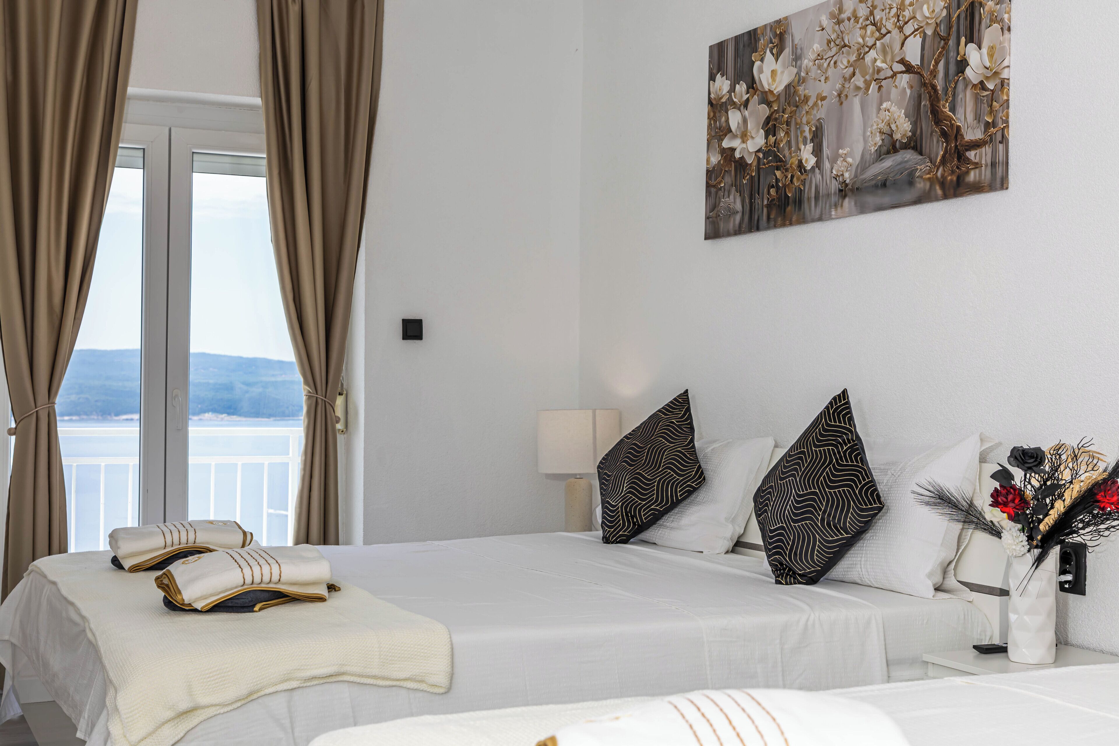 Ein Hotelzimmer mit Bett, Vorhängen, einem Gemälde und einer Blumenvase.