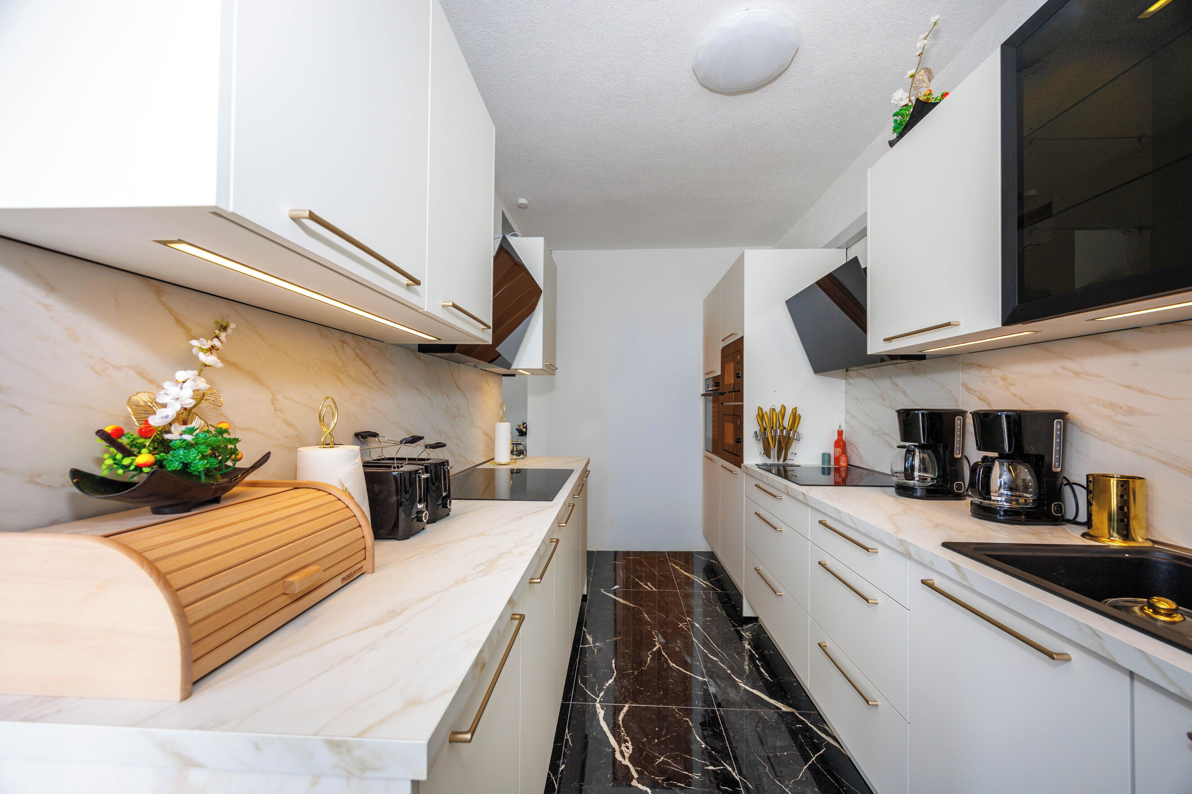 A modern kitchen with white cabinetry, a marble countertop, and a black tiled floor.