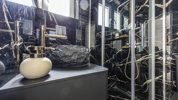 Un baño moderno con lavamanos de mármol, grifería cromada y cabina de ducha con paredes de vidrio.