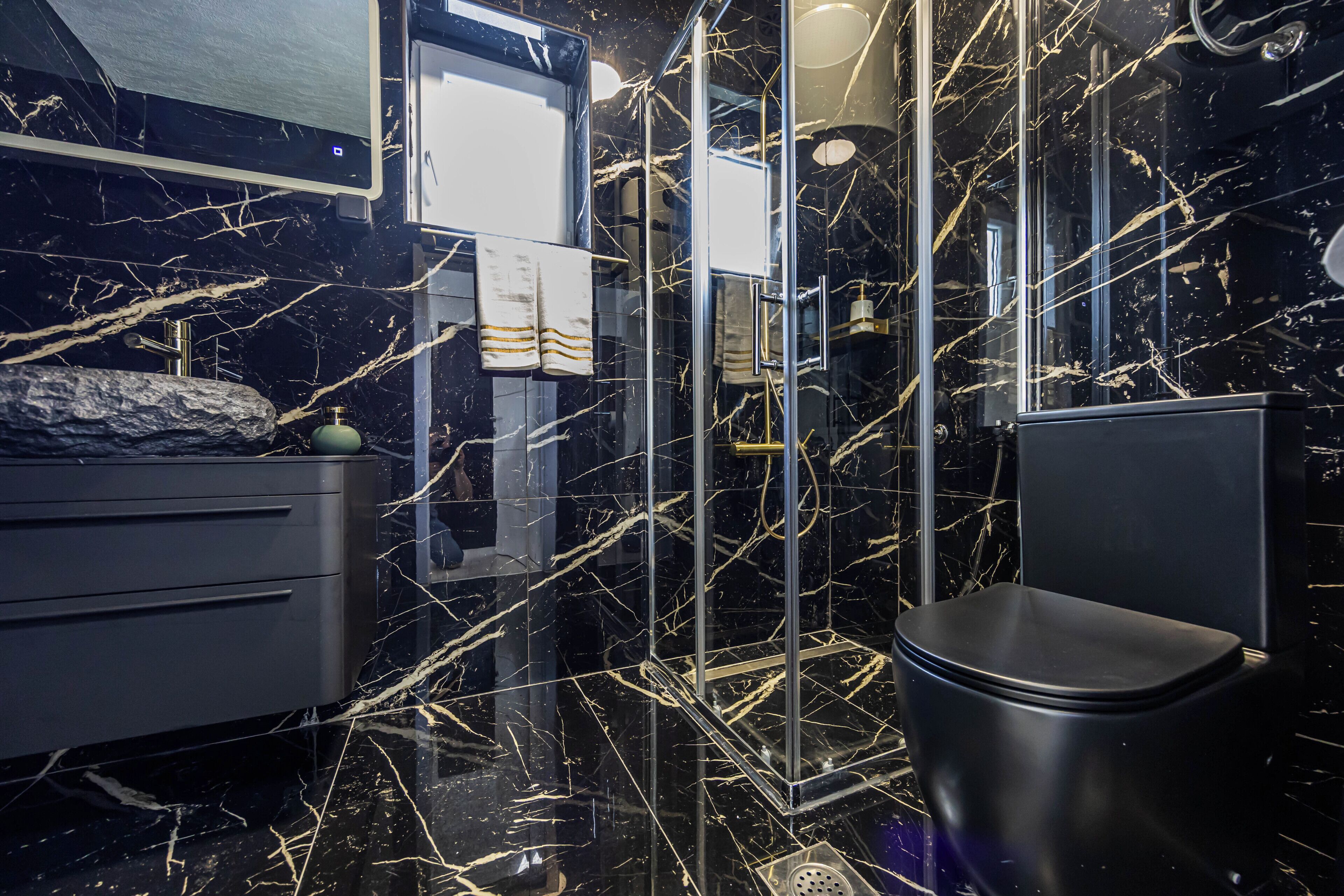 A bathroom with a black marble floor, a black toilet, a mirror, and a sink with a modern design.