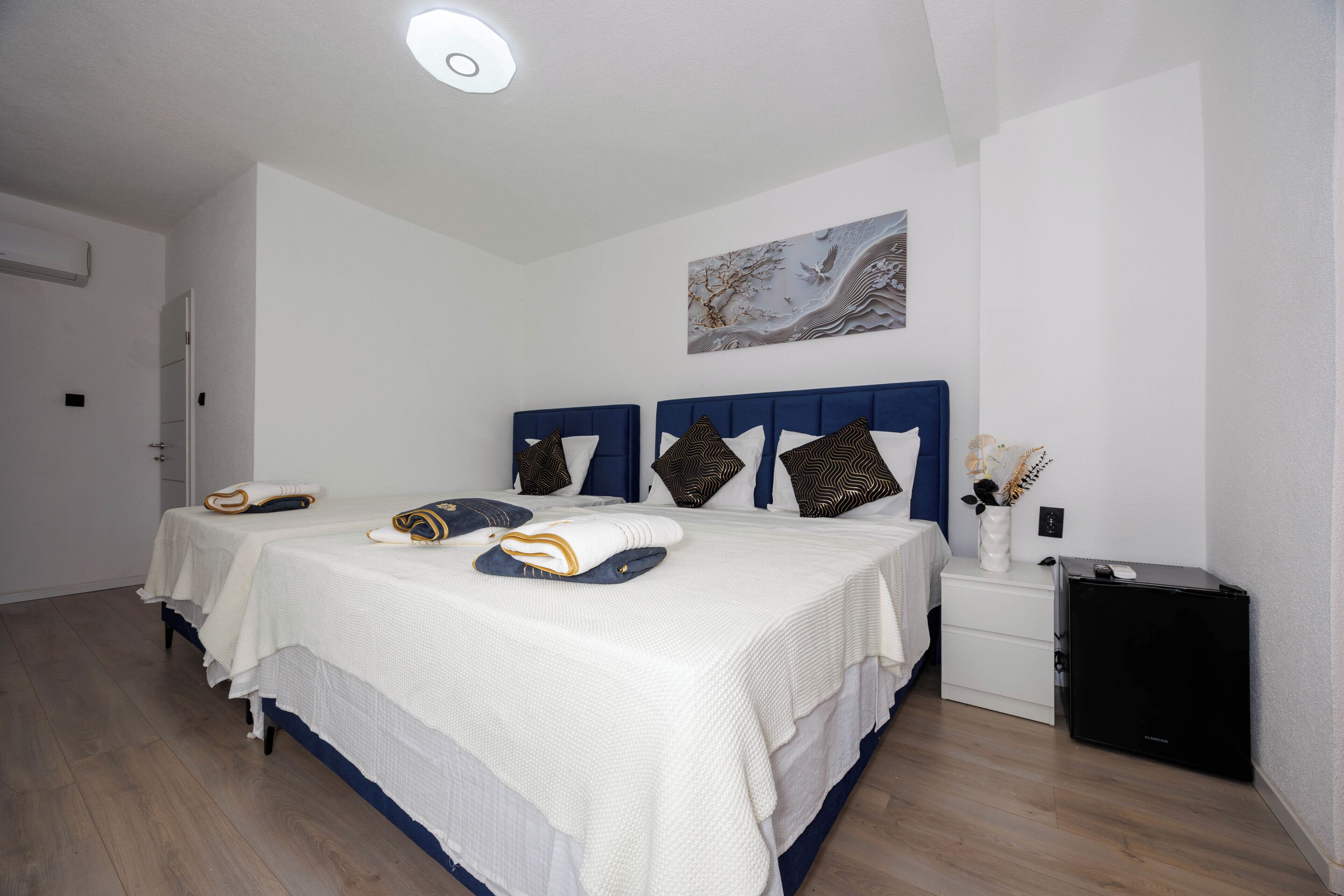 A bedroom with two beds, a nightstand, a small black cabinet, and a wall-mounted artwork.