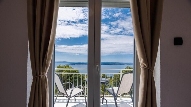 Un balcón con vistas al mar y a las montañas, una mesa y dos sillas.