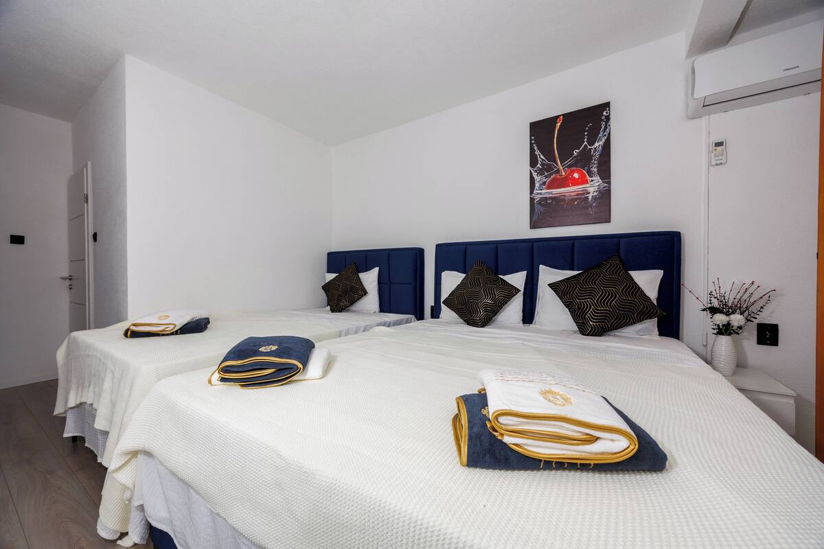 Una habitación de hotel con dos camas, ropa de cama blanca, cabeceros azules y almohadas decorativas.