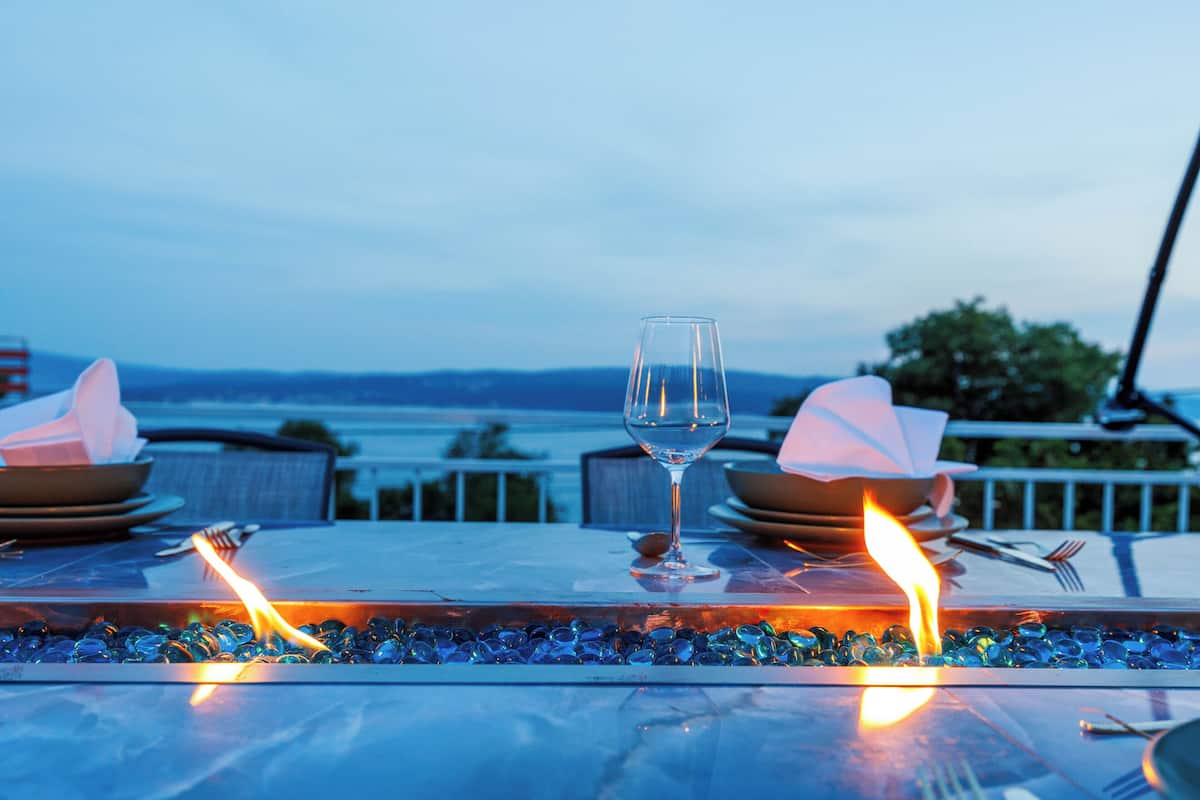 Una mesa con un vaso de agua, platos y cubiertos, frente a una vista del agua y el paisaje distante.