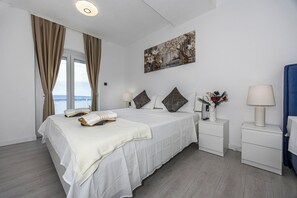Une chambre d’hôtel avec un lit, deux tables de chevet, une commode, un tableau et une vue sur la mer.