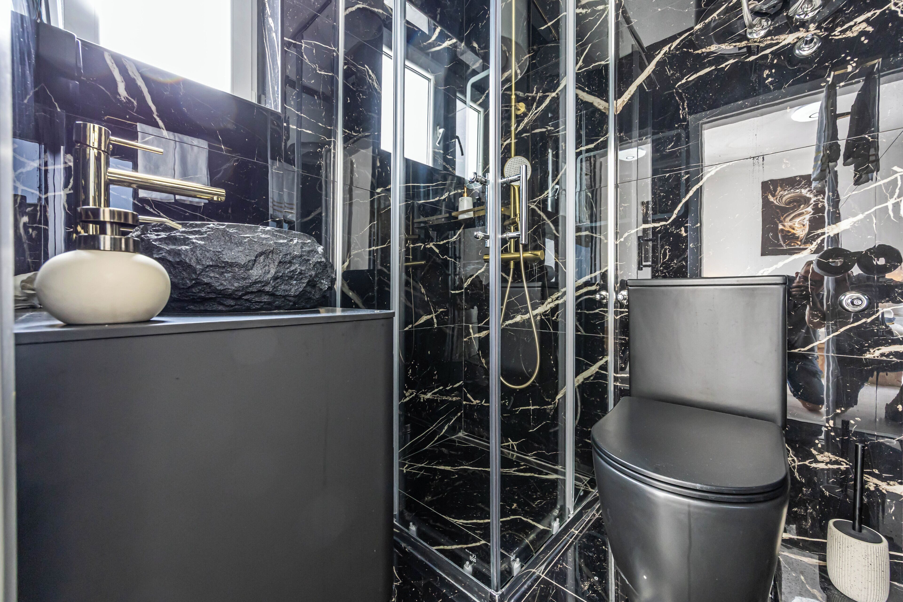 Un baño con lavamanos de mármol negro, un lavabo blanco de pedestal, inodoro negro y zona de ducha con mampara de vidrio.