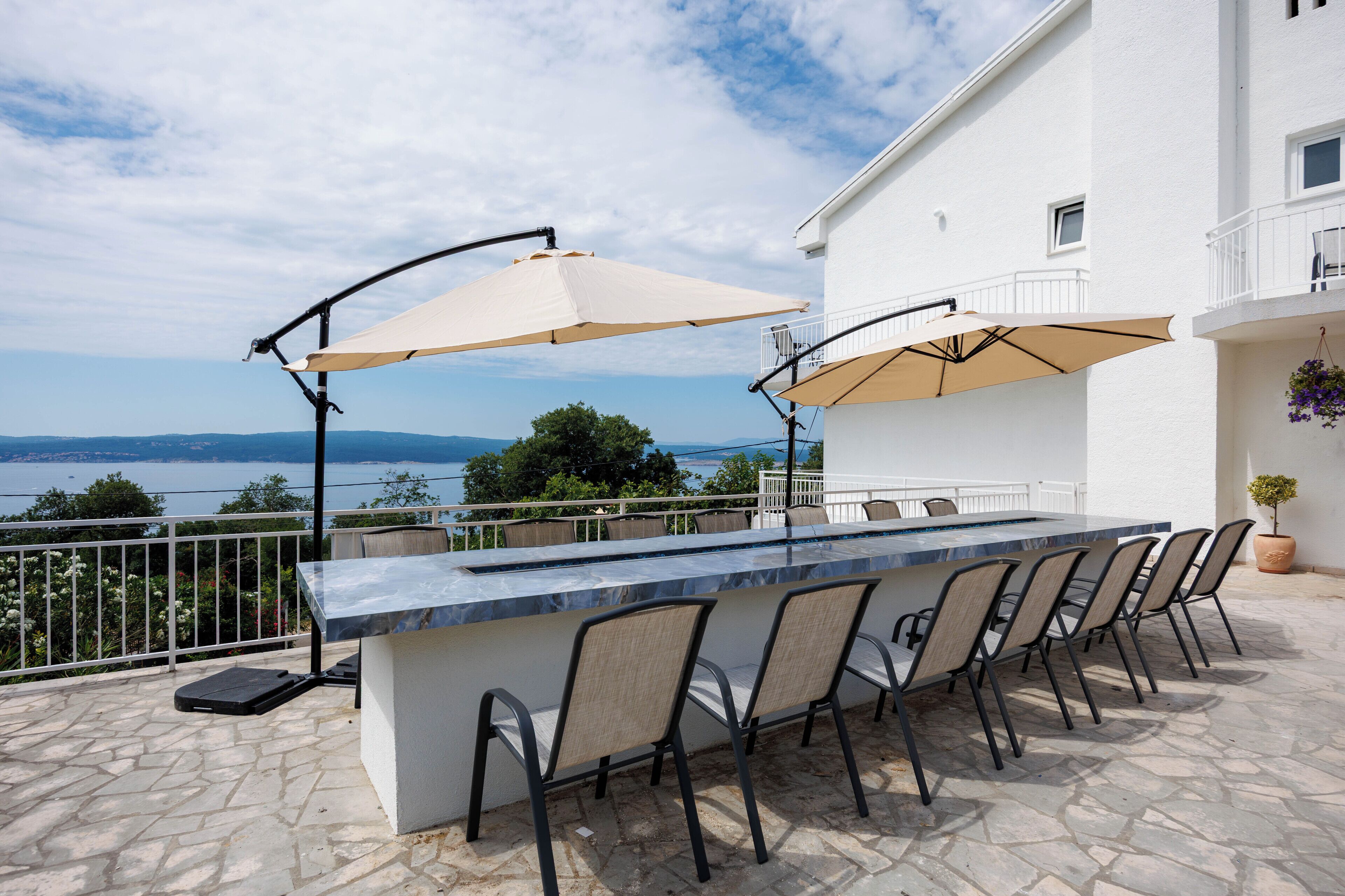 An outdoor bar area with a stone floor, a long counter, and multiple chairs.