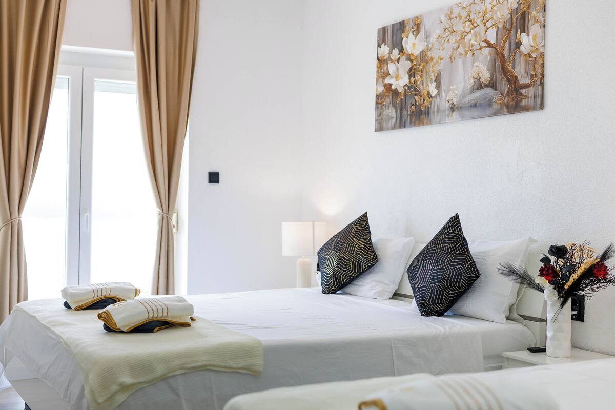 Habitación de hotel con cama, dos almohadas, mesita de noche con un jarrón y un cuadro en la pared.
