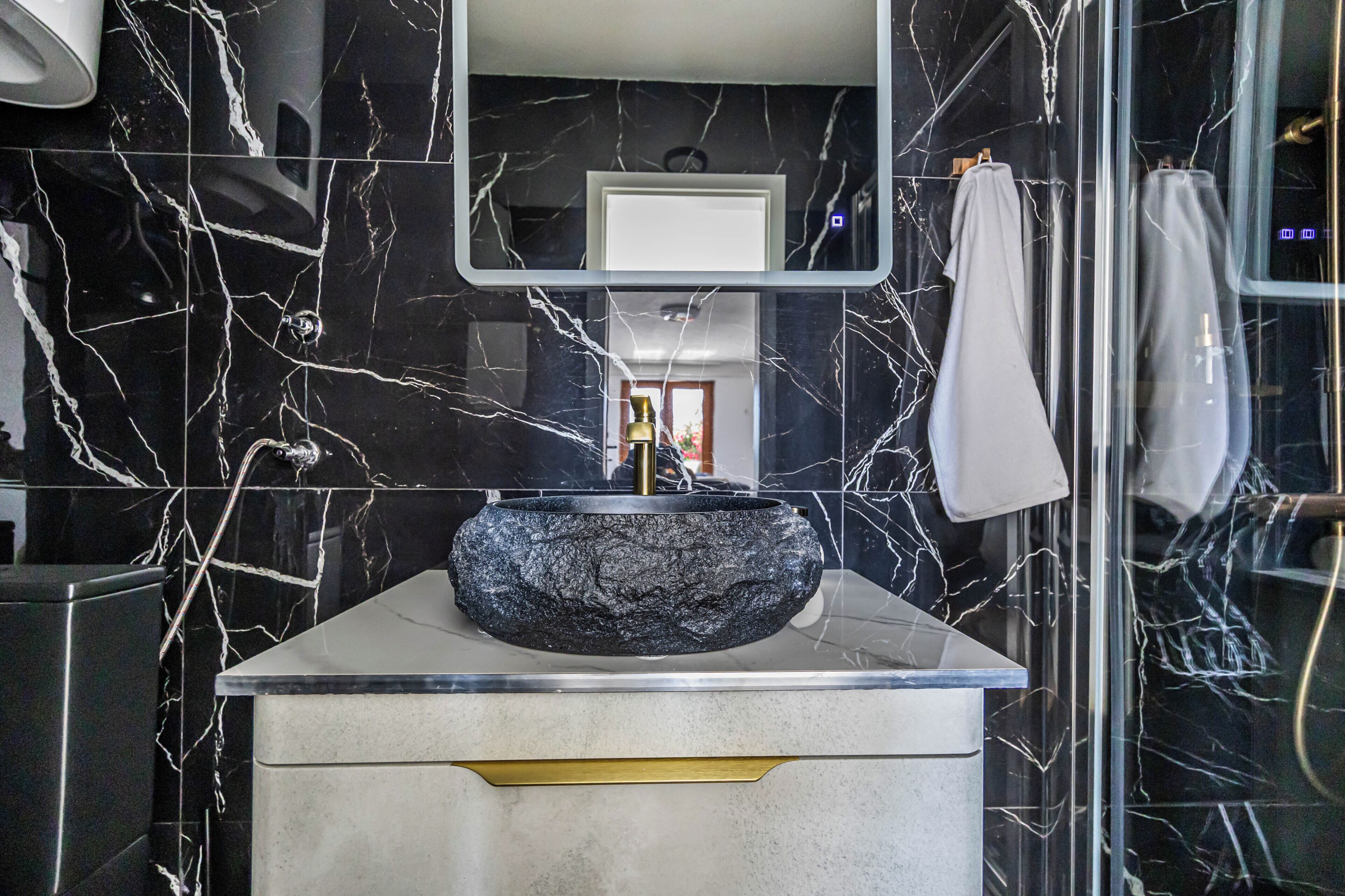 Casa de banho com lavatório de mármore preto, bancada branca e espelho em cima.