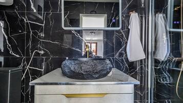 Casa de banho com lavatório de mármore preto, bancada branca e espelho em cima.