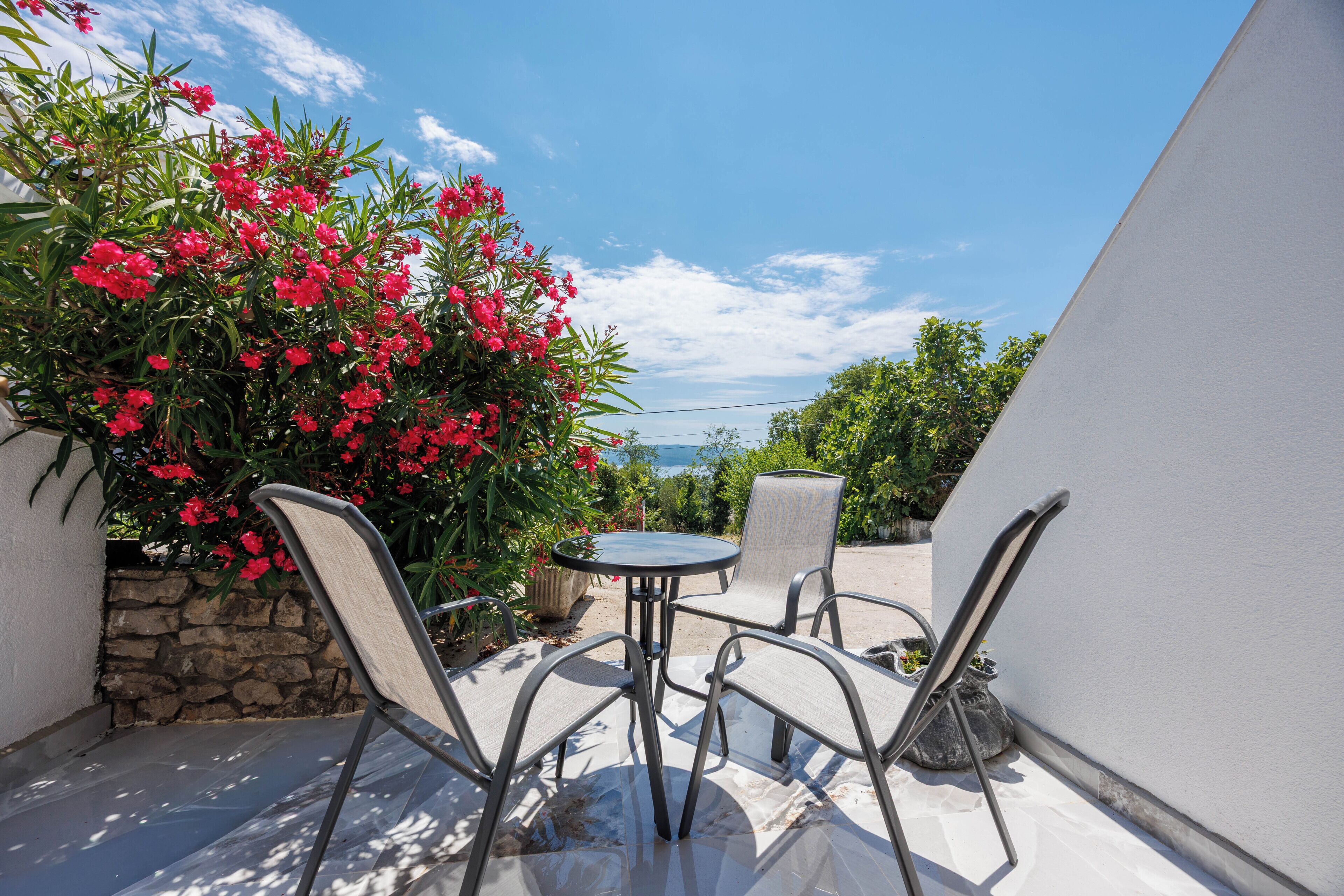 A patio with a table and chairs, surrounded by plants and a stone wall.