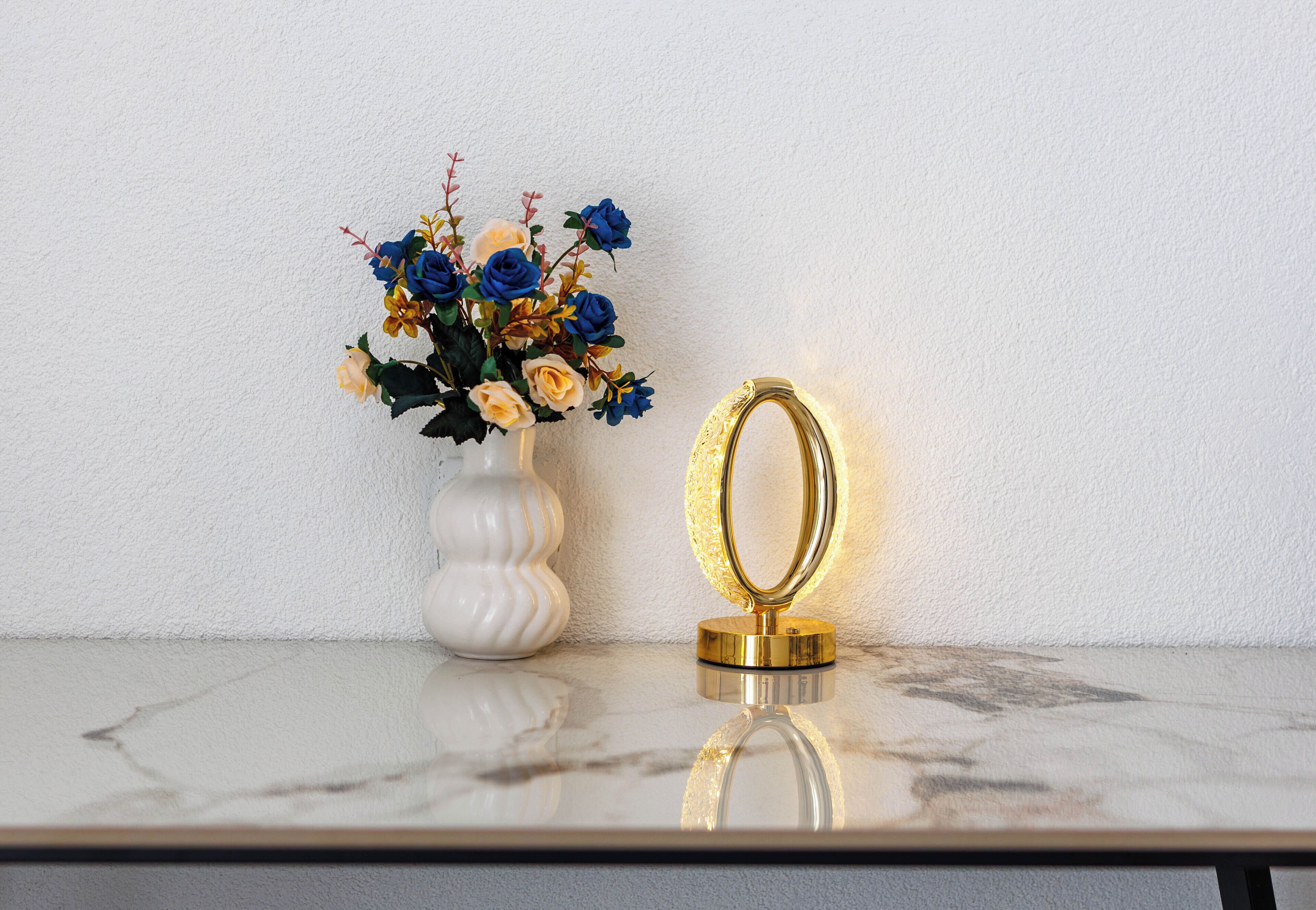 Un vase blanc orné de fleurs et un miroir à cadre doré, posés sur une surface en marbre.