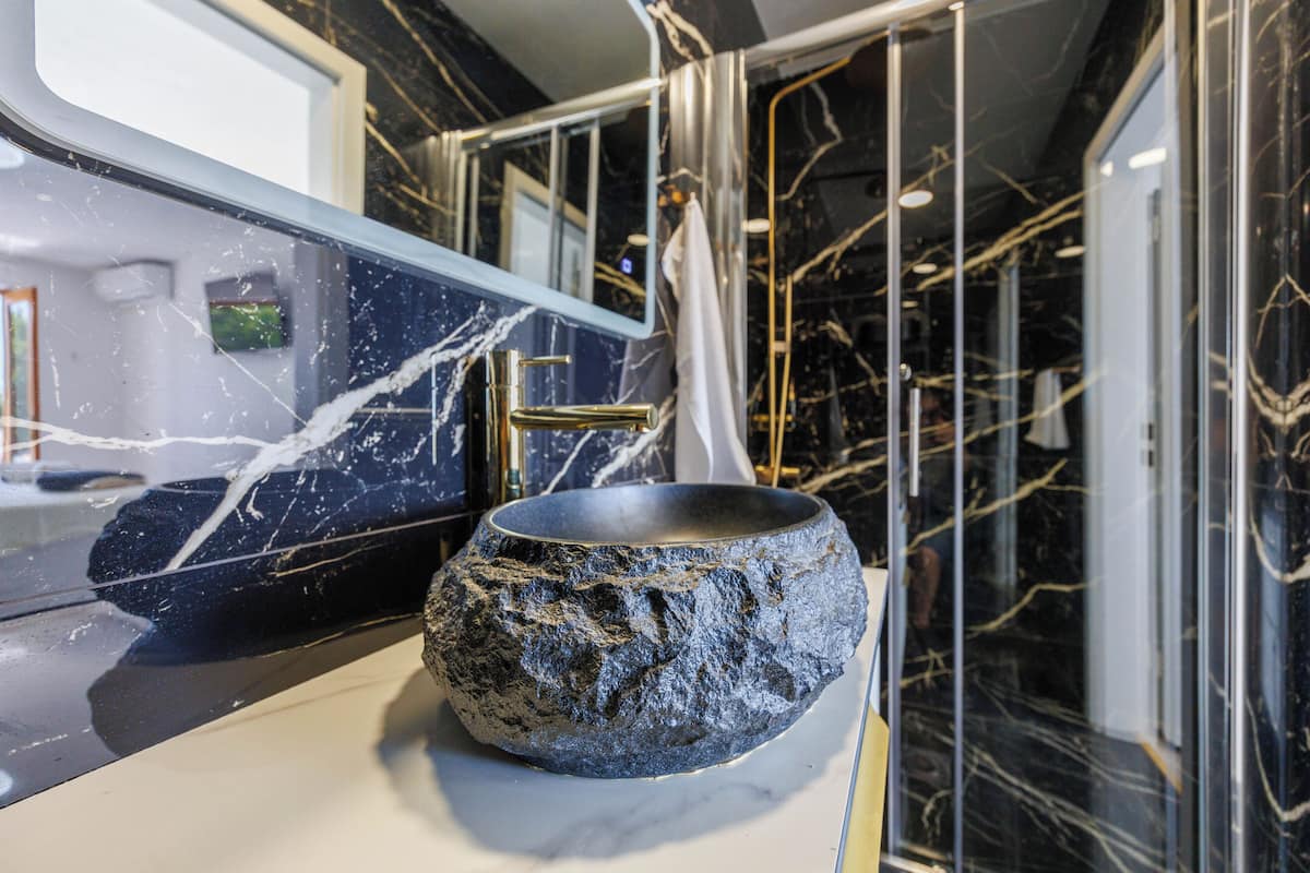 Un baño con lavamanos de mármol, grifo dorado y cabina de ducha de vidrio.