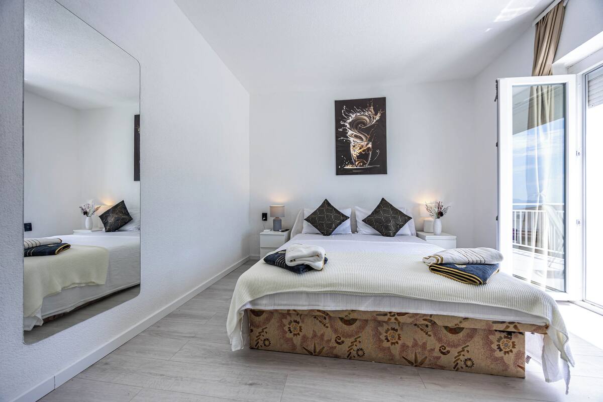 Un dormitorio moderno con una cama grande, un espejo, un cuadro y un balcón.