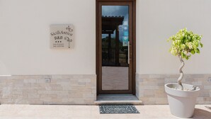 A building entrance with a door, a potted tree, and a signboard. - Room 'Maidda' with Shared Garden, Wi-Fi and Air Conditioning (Rilievo)