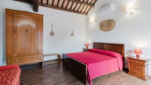 A bedroom with a wooden wardrobe, a bed with a red bedspread, a nightstand with a lamp, and a ceiling fan. - Studio 'Zirafa' with Shared Garden, Wi-Fi and Air Conditioning (Rilievo)