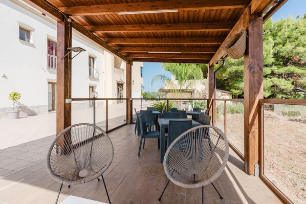 An outdoor patio with wooden beams, wicker chairs, and tables.