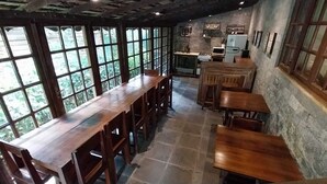A rustic dining area with wooden tables and chairs, large windows, and a kitchen in the background. - Hospedagem Country Inn  (Nova Friburgo)