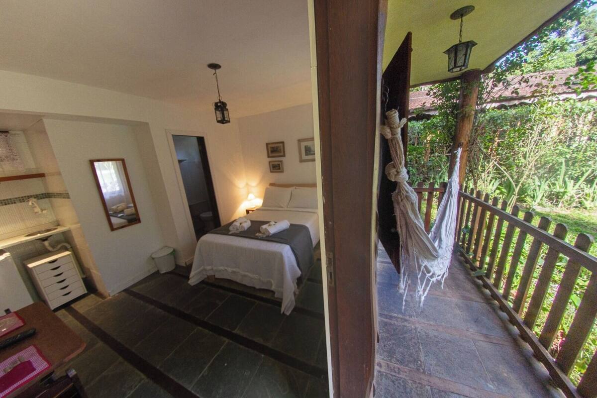 Un dormitorio con cama, lámpara de noche y vistas a un jardín desde un balcón.