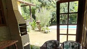 An outdoor patio with a brick wall, a grill, wicker furniture, and a view of greenery. - Hospedagem Country Inn  (Nova Friburgo)