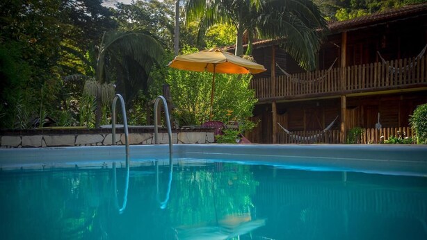 A swimming pool with a wooden deck and a wooden building in the background. - Hospedagem Country Inn  (Nova Friburgo)