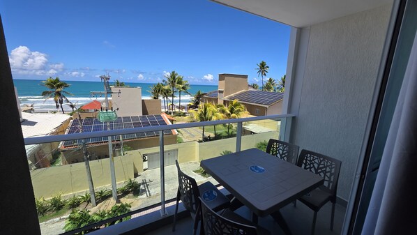 A balcony with a table and chairs, overlooking a beach with palm trees and a view of the ocean.
