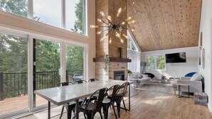 Amplia sala de estar con una gran mesa de comedor, sillas modernas, una chimenea y un televisor montado en la pared.