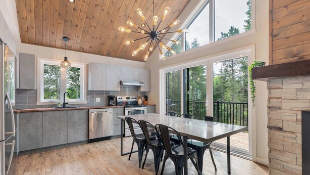 Una cocina moderna con techo de madera, ventanas amplias y una zona de comedor con sillas.