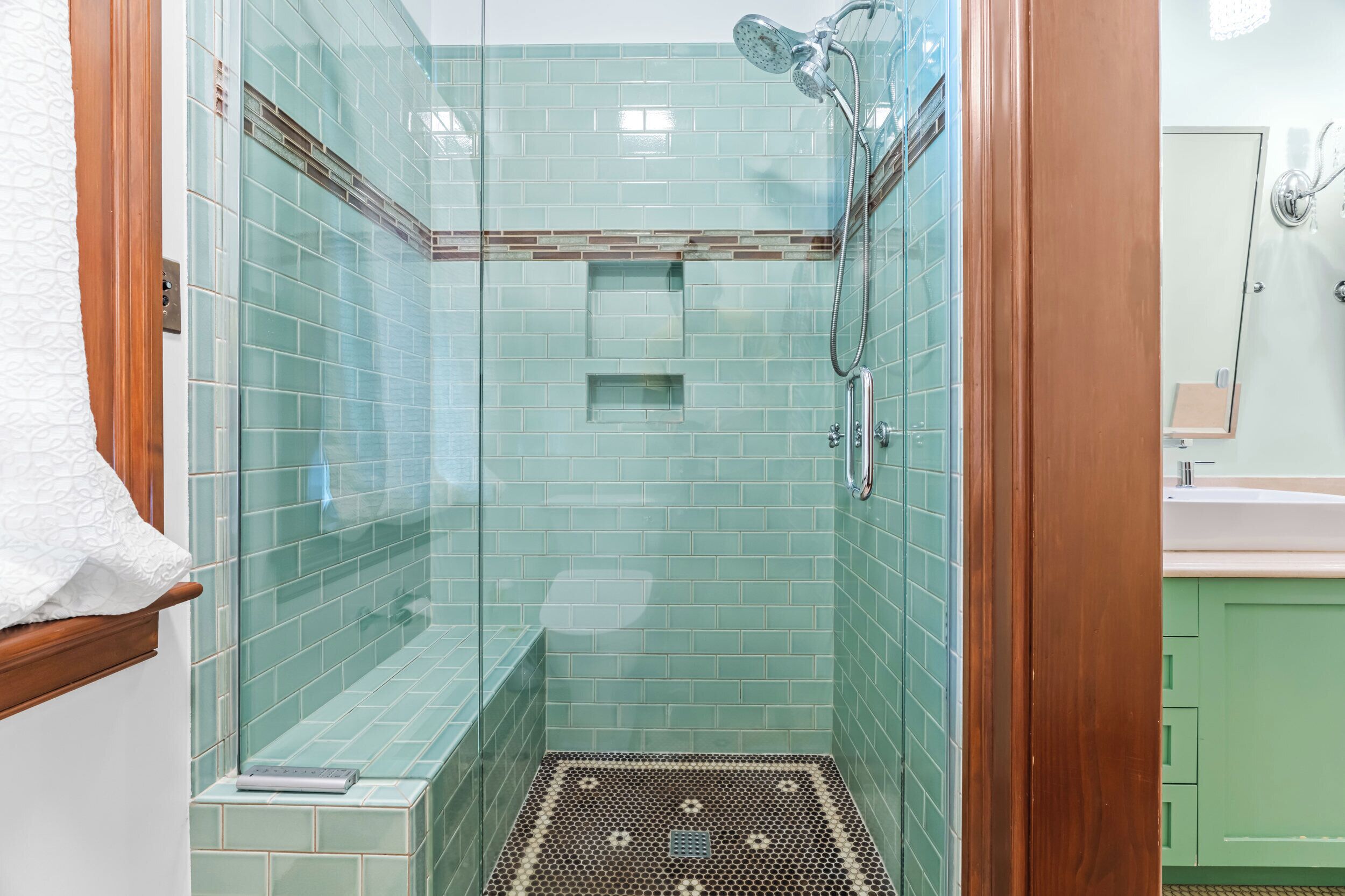 A glass-enclosed shower with a tiled floor, a handheld showerhead, and a control panel.
