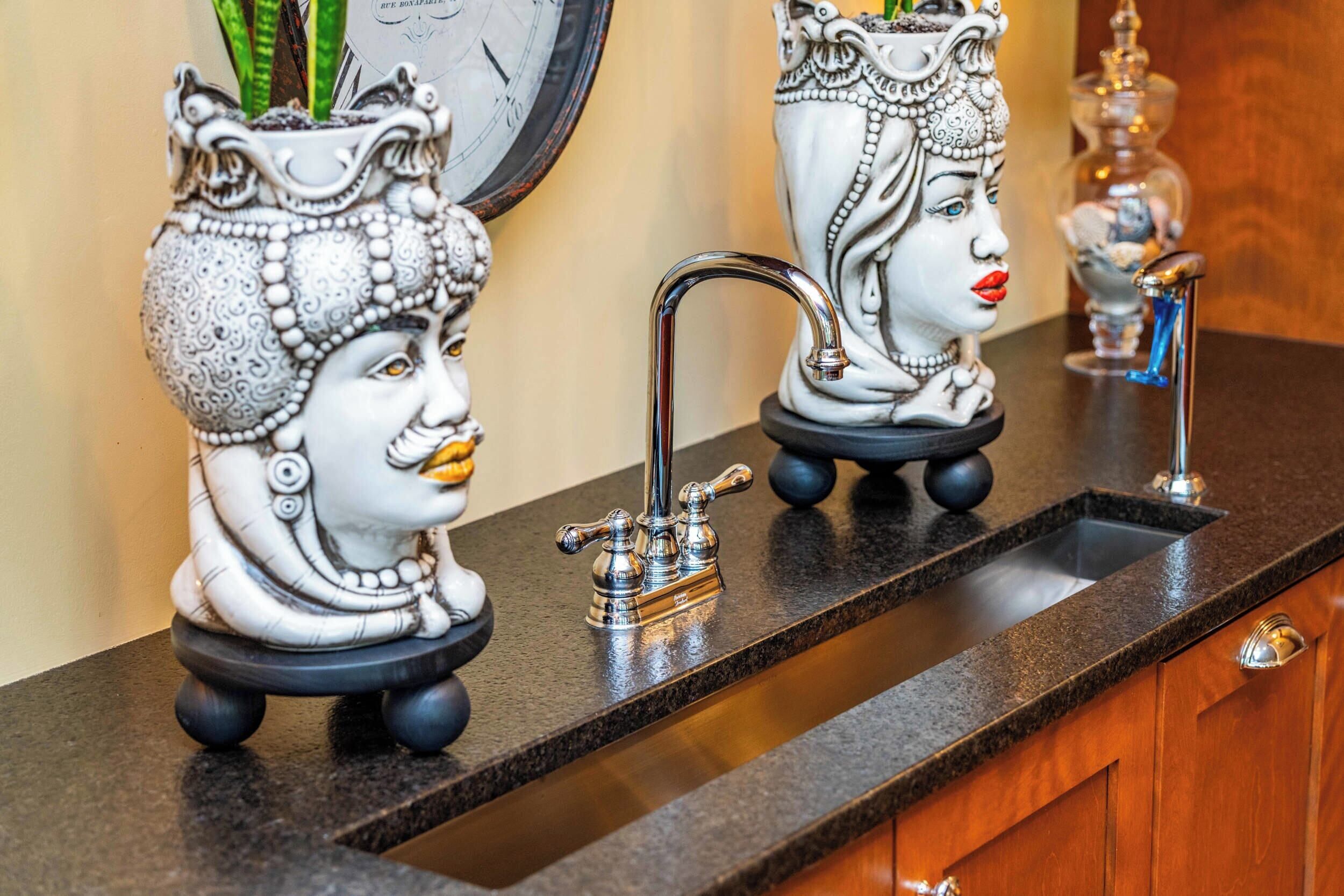 Un comptoir de cuisine orné de trois vases en céramique décoratifs, chacun représentant un visage, ainsi qu’un robinet et une horloge murale.