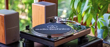 A turntable with a wooden cabinet and speakers, placed on a table near a window with a view of greenery.