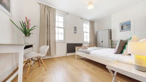 Quarto com cama, mesa de cabeceira, cadeira e um vaso de plantas.