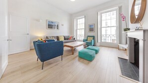 Uma sala de estar ampla, com um sofá, poltronas, uma mesa de centro e lareira.