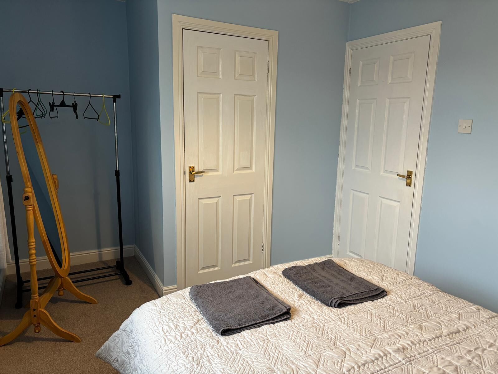 A bedroom with a bed, two doors, and a wooden hanger stand.